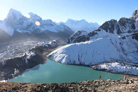 A trekker on Gokyo Ri gazing at the turquoise Gokyo Lake with Cholatse peak rising in the distance